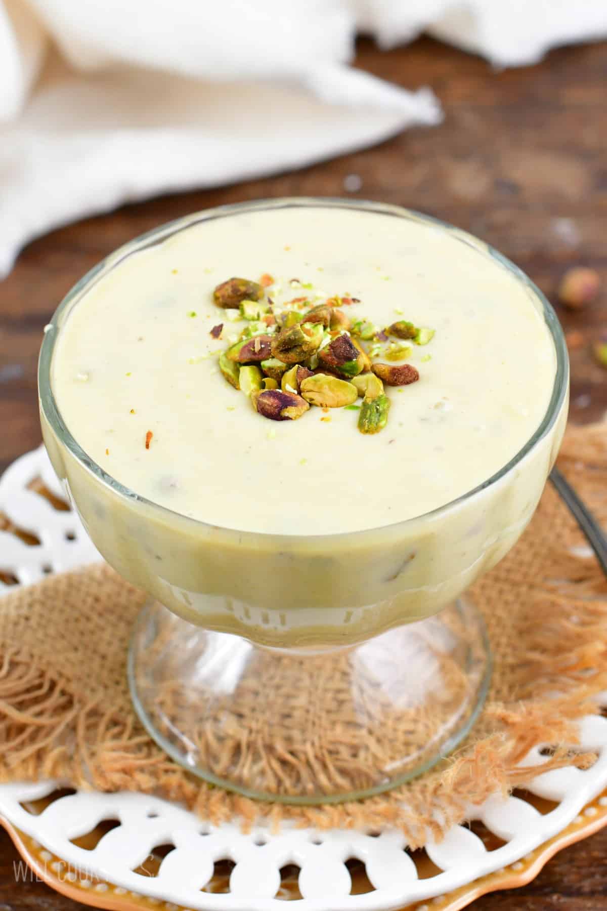 pistachio pudding in a serving bowl on a burlap napkin on a white plate.