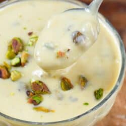 Pistachio pudding in a bowl with pistachios on top and a spoon scooping some out.