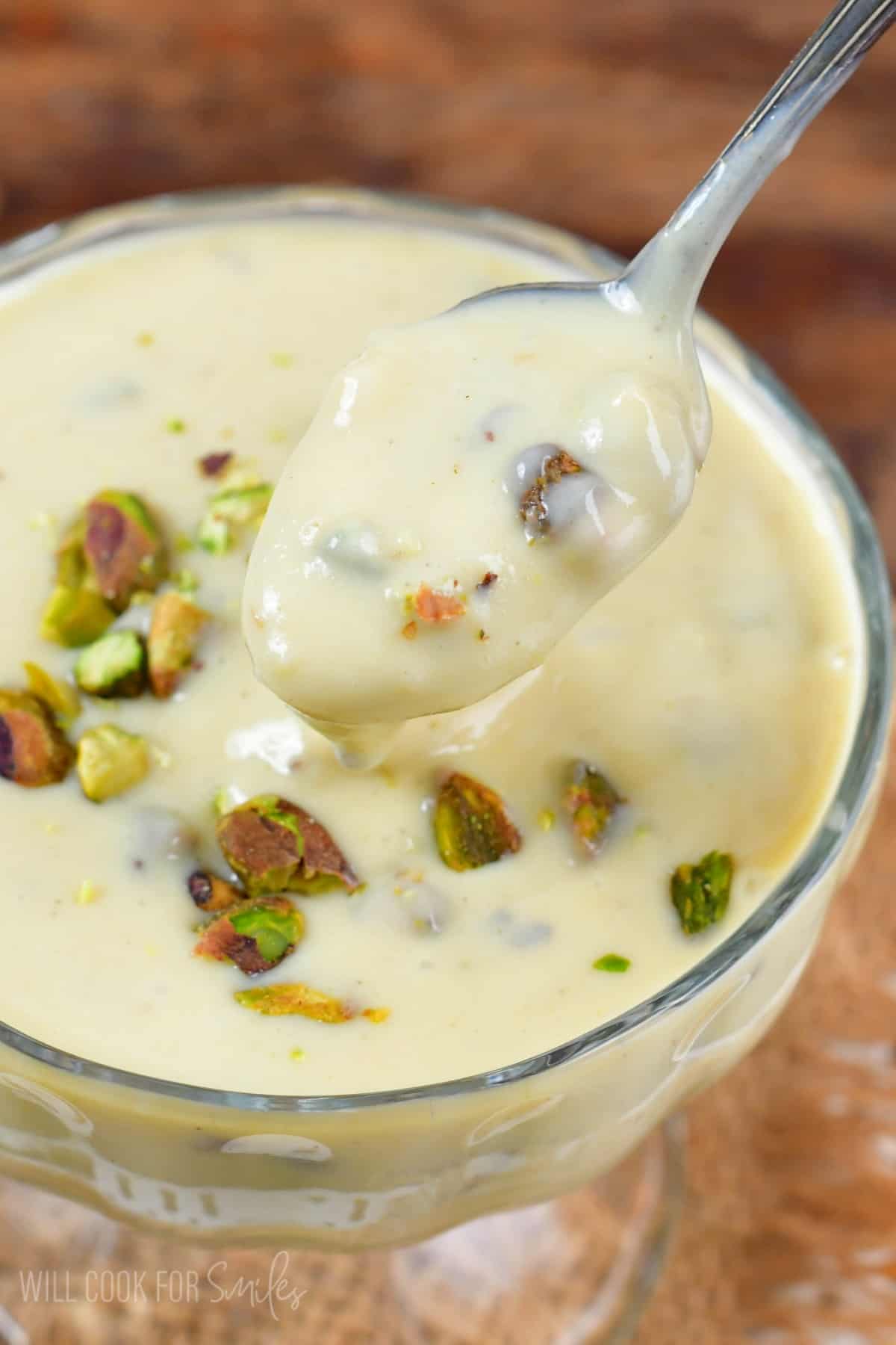 Pistachio pudding in a bowl with pistachios on top and a spoon scooping some out.