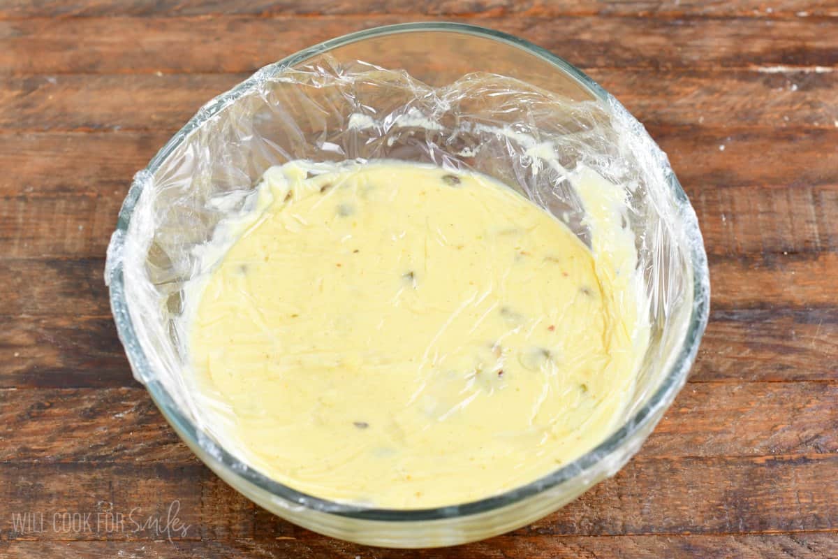 pistachio pudding in a bowl with plastic wrap covering pushed down into the pudding and wrapped around the bowl.