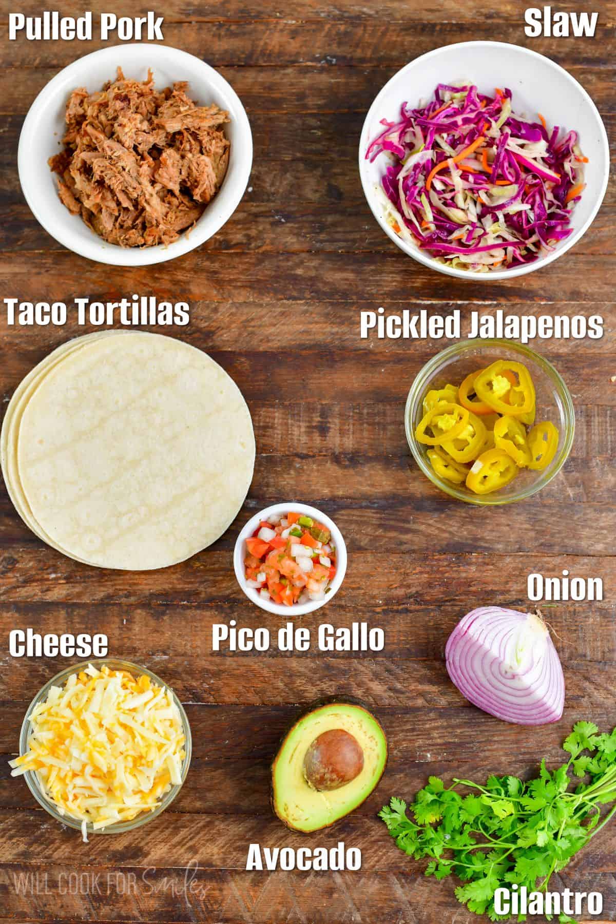 Labeled ingredients for pulled pork tacos on a wood surface.
