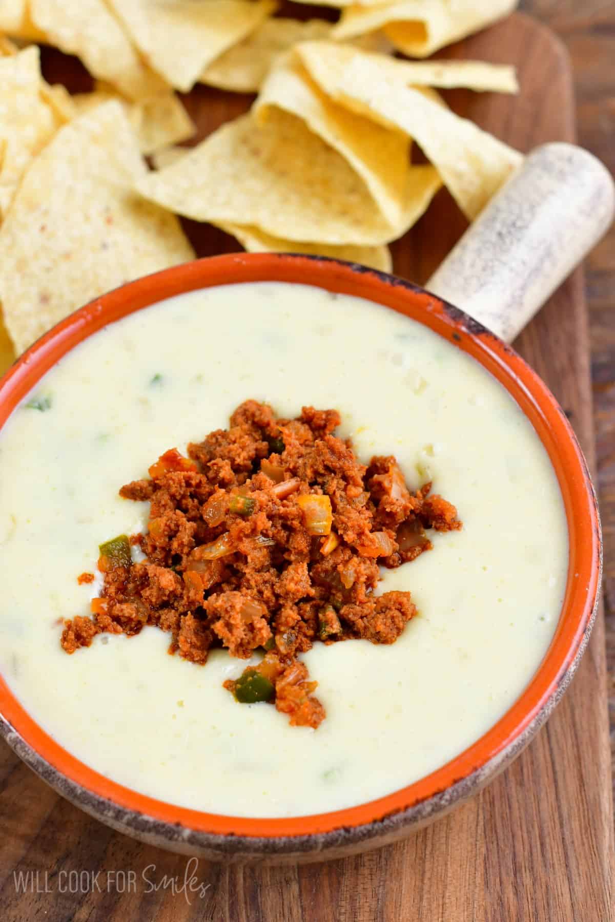 a bowl with a handle filled with queso blanco dip and topped with Mexican chorizo sausage.