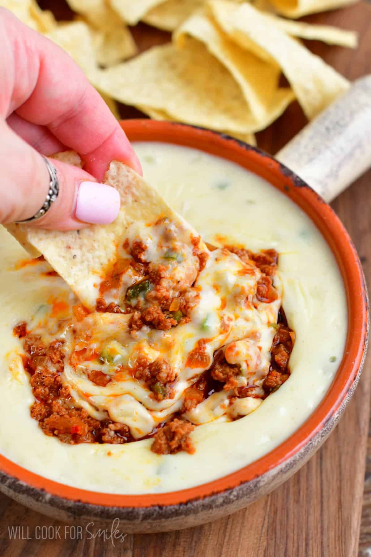 scooping some queso dip swirled with chorizo sausage using tortilla chip. 