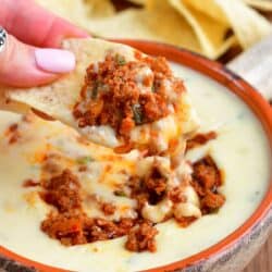 holding some queso dip and chorizo on a tortilla chip.