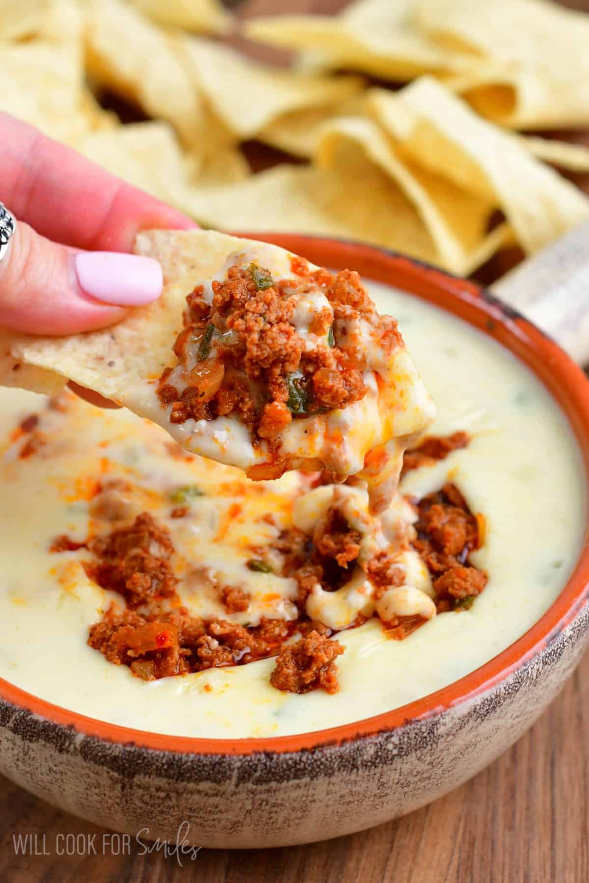 holding some queso dip and chorizo on a tortilla chip.