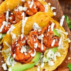 three shrimp tacos on a plate with avocado, cheese, and creme on top.