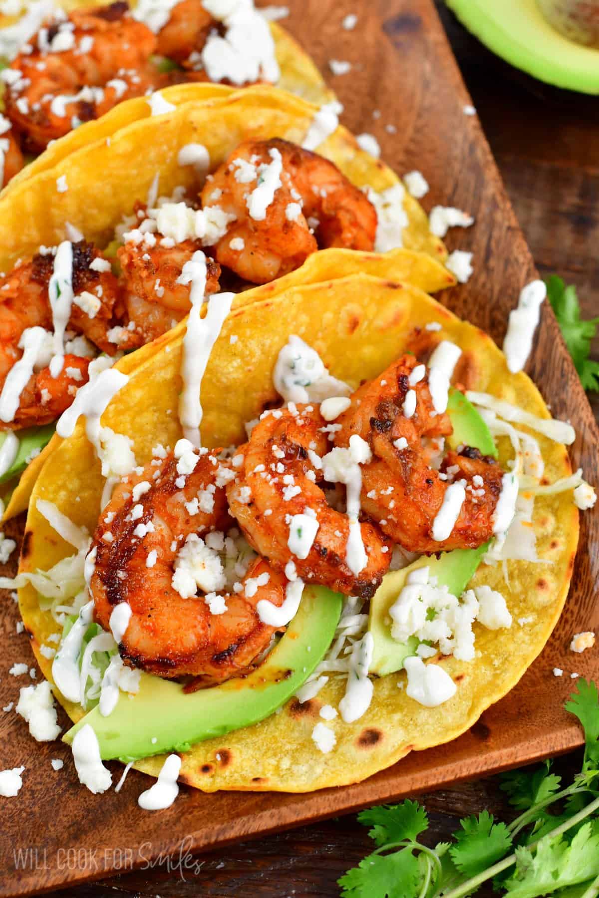 three shrimp tacos on a plate with avocado, cheese, and creme on top.