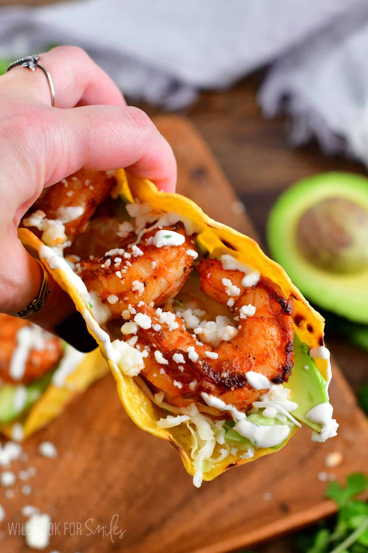 Holding a shrimp taco with a wood plate in the background.