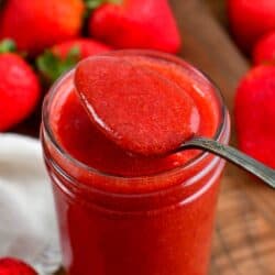 Spooning Strawberry sauce out of a mason jar with strawberries around them.