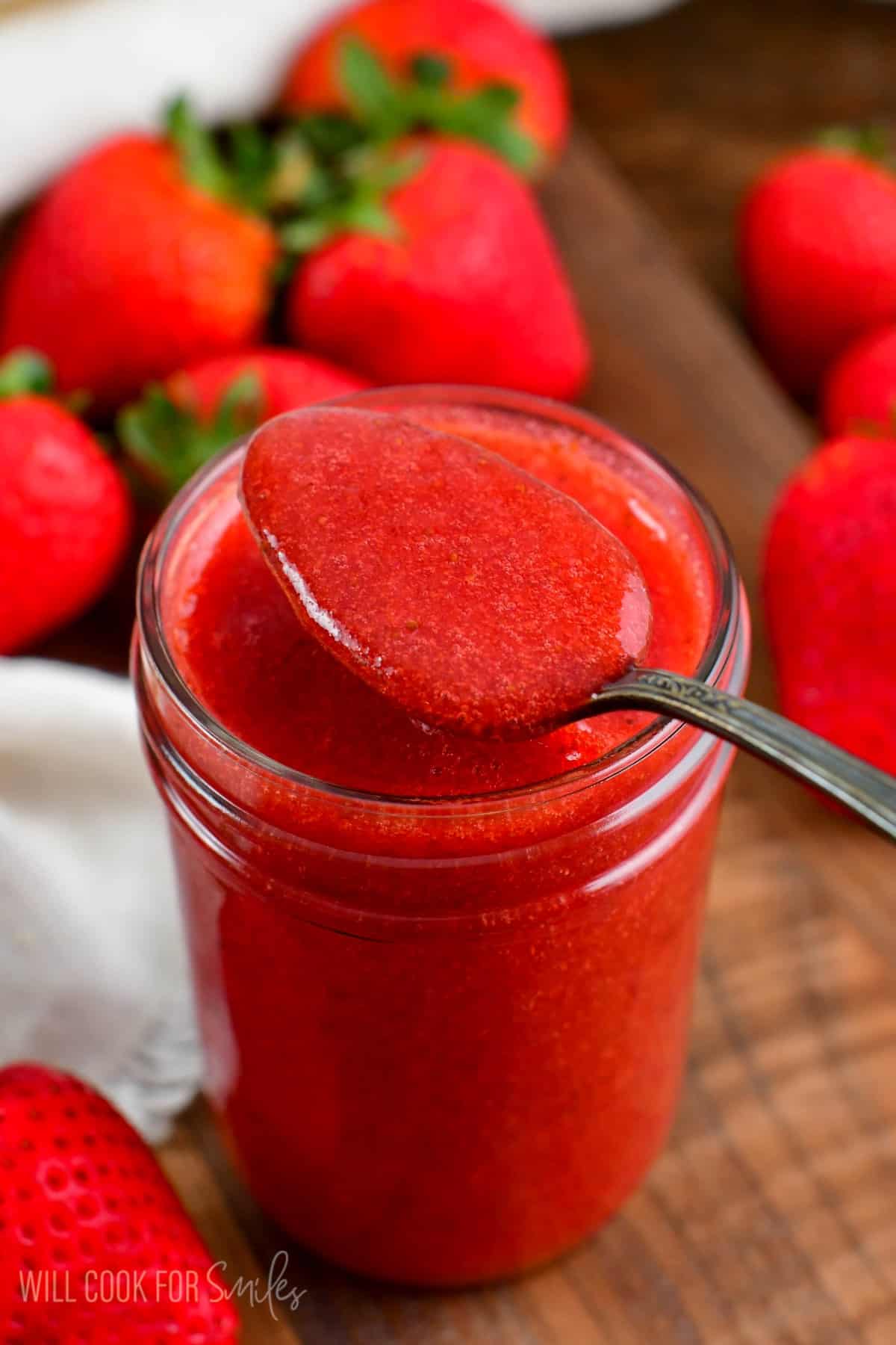 Spooning Strawberry sauce out of a mason jar with strawberries around them.