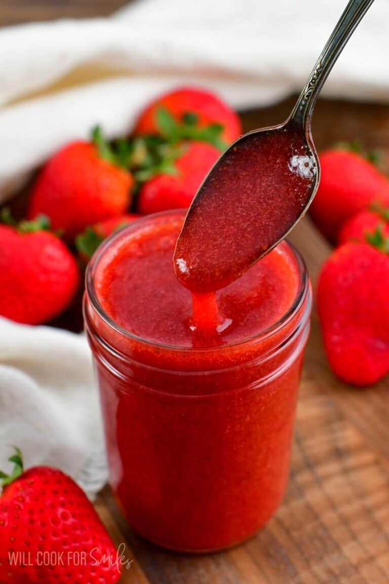 Spooning strawberry sauce our of jar with a little spoon.