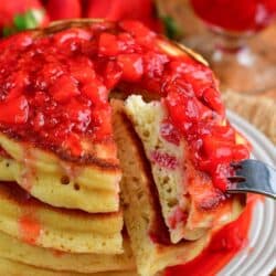 Cutting a bite out of the stack of strawberry pancakes with a fork.