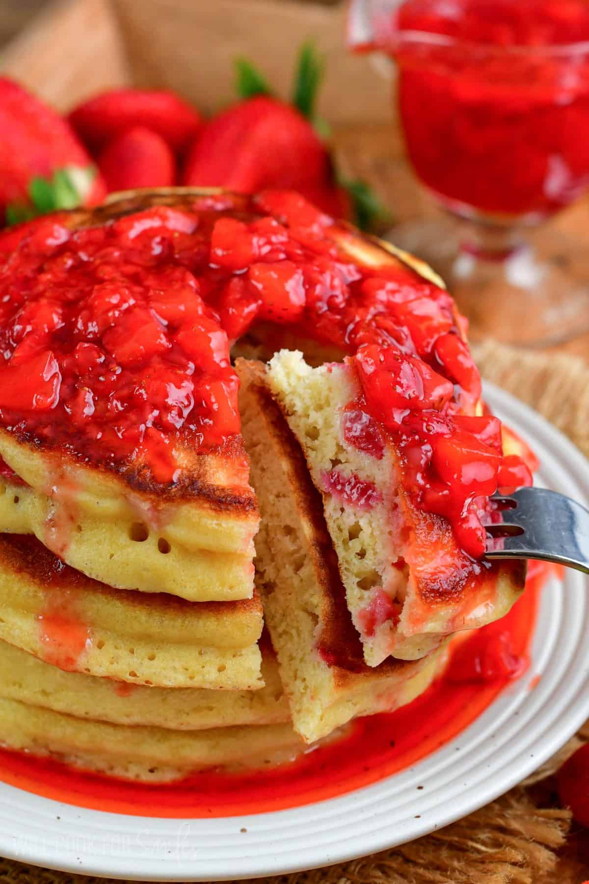 Cutting a bite out of the stack of strawberry pancakes with a fork.