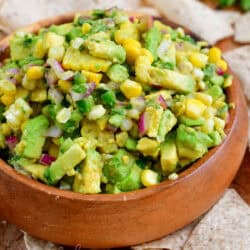 wooden bowl full of avocado salsa surrounded by light tortilla chips.