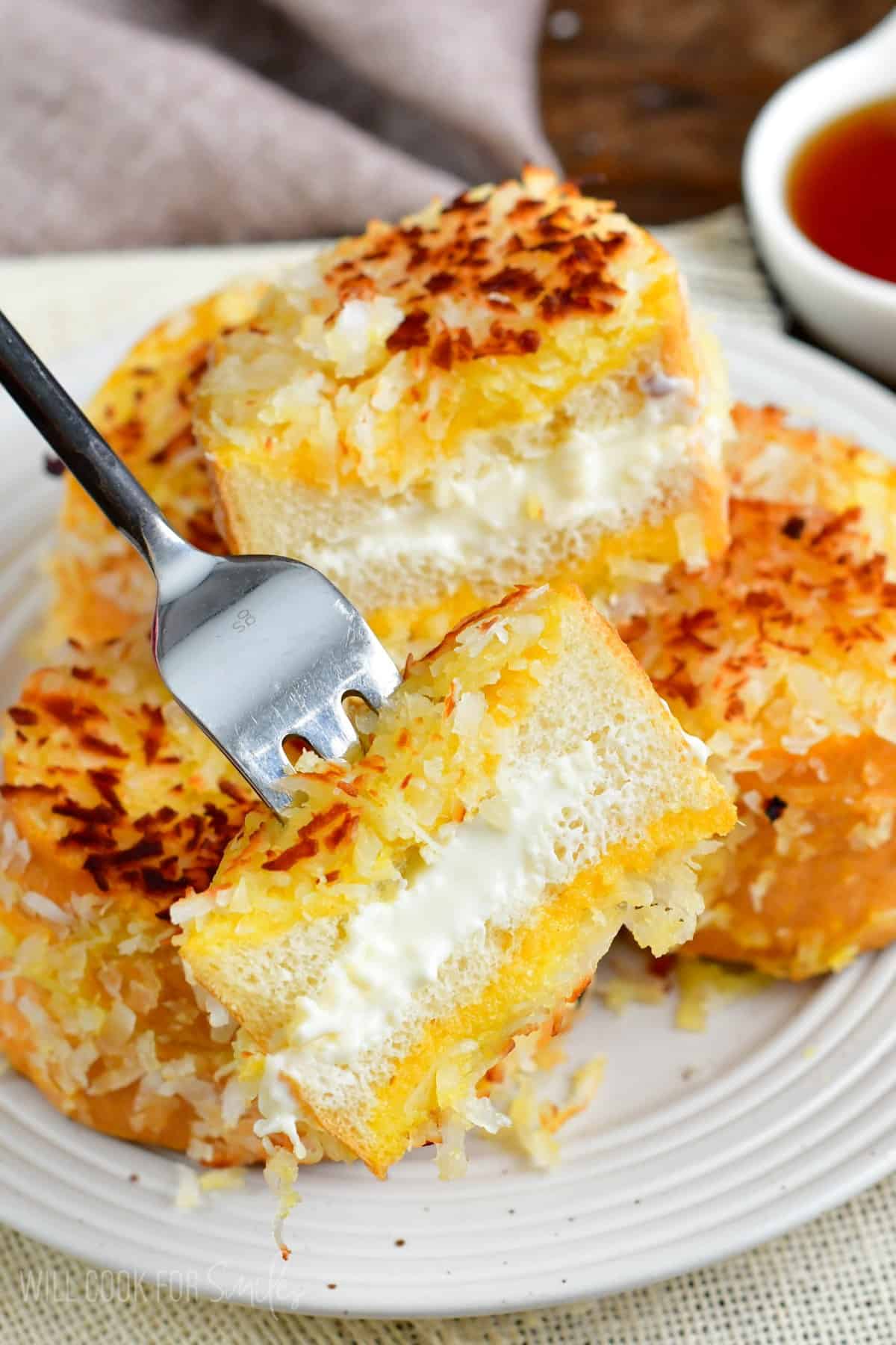 sliced coconut stuffed French toast on a fork and more on the plate.