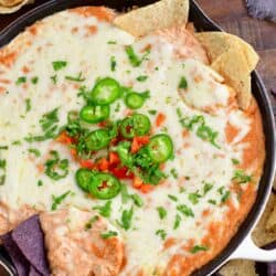 hot bean dip topped with tomatoes, jalapenos, and cilantro in a cast iron skillet with some tortilla chips in it.