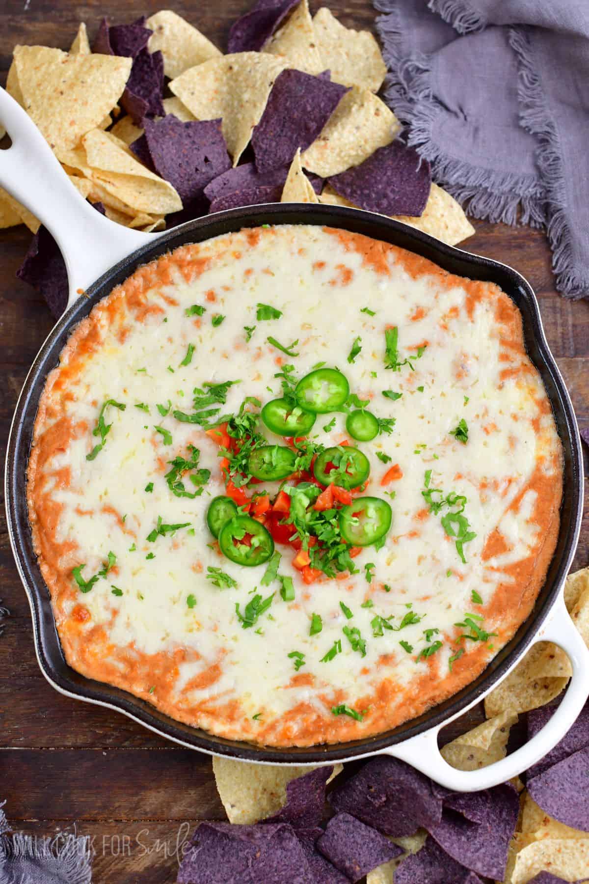 hot bean dip topped with tomatoes, jalapenos, and cilantro in a cast iron skillet.
