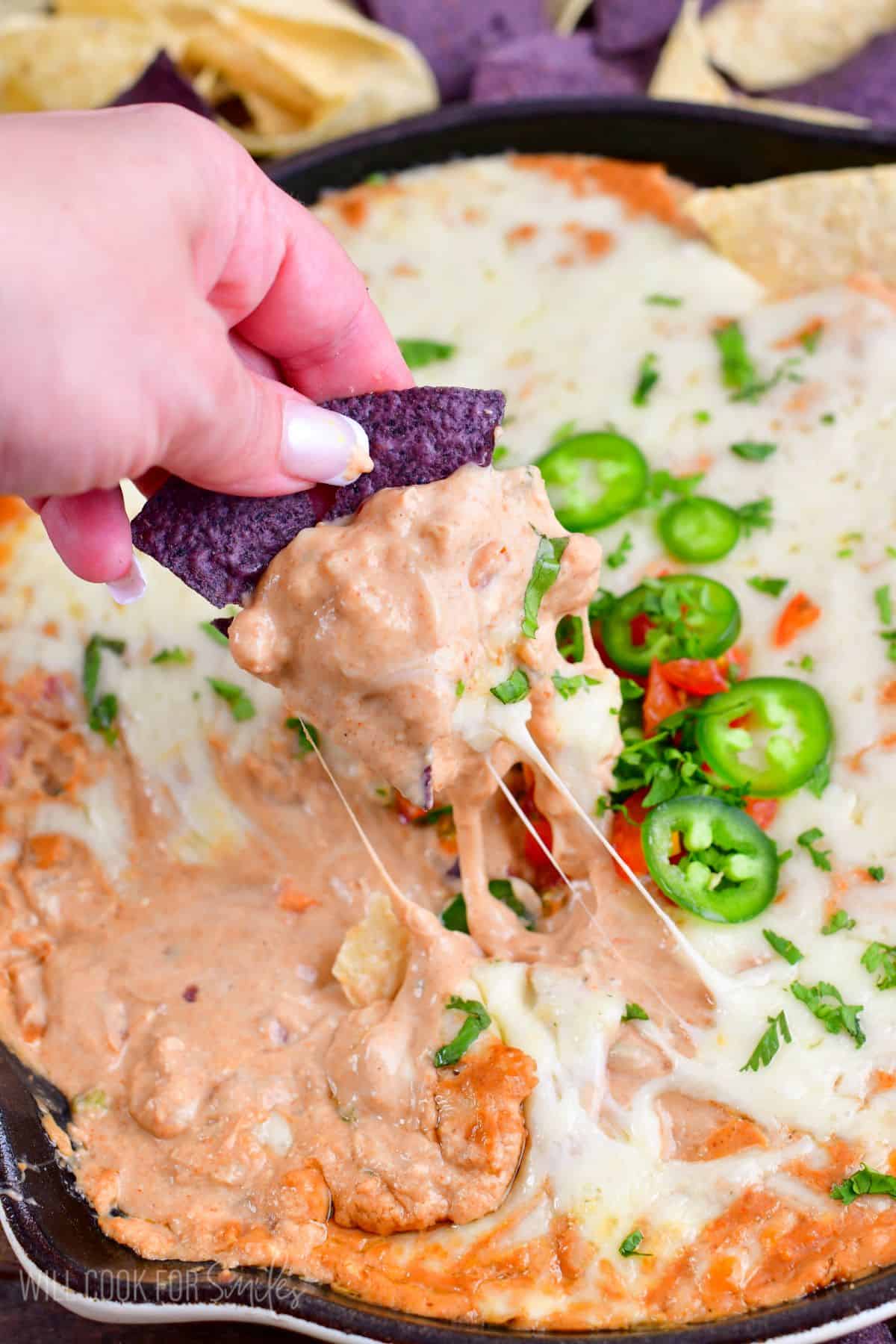 scooping hot bean dip with some tortilla chips from the skillet.