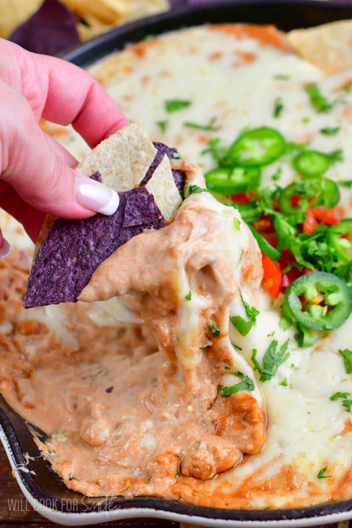 scooping hot bean dip from a cast iron skillet using tortilla chips.