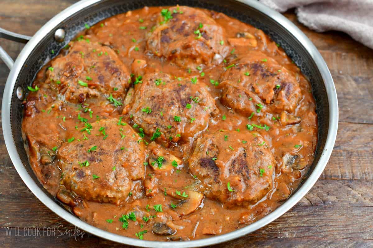 Salisbury steaks in a pan with gravy on a wood surface.