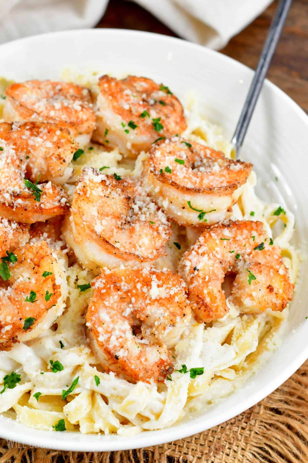 Shrimp alfredo in a white bowl on a burlap tablecloth underneath the bowl.