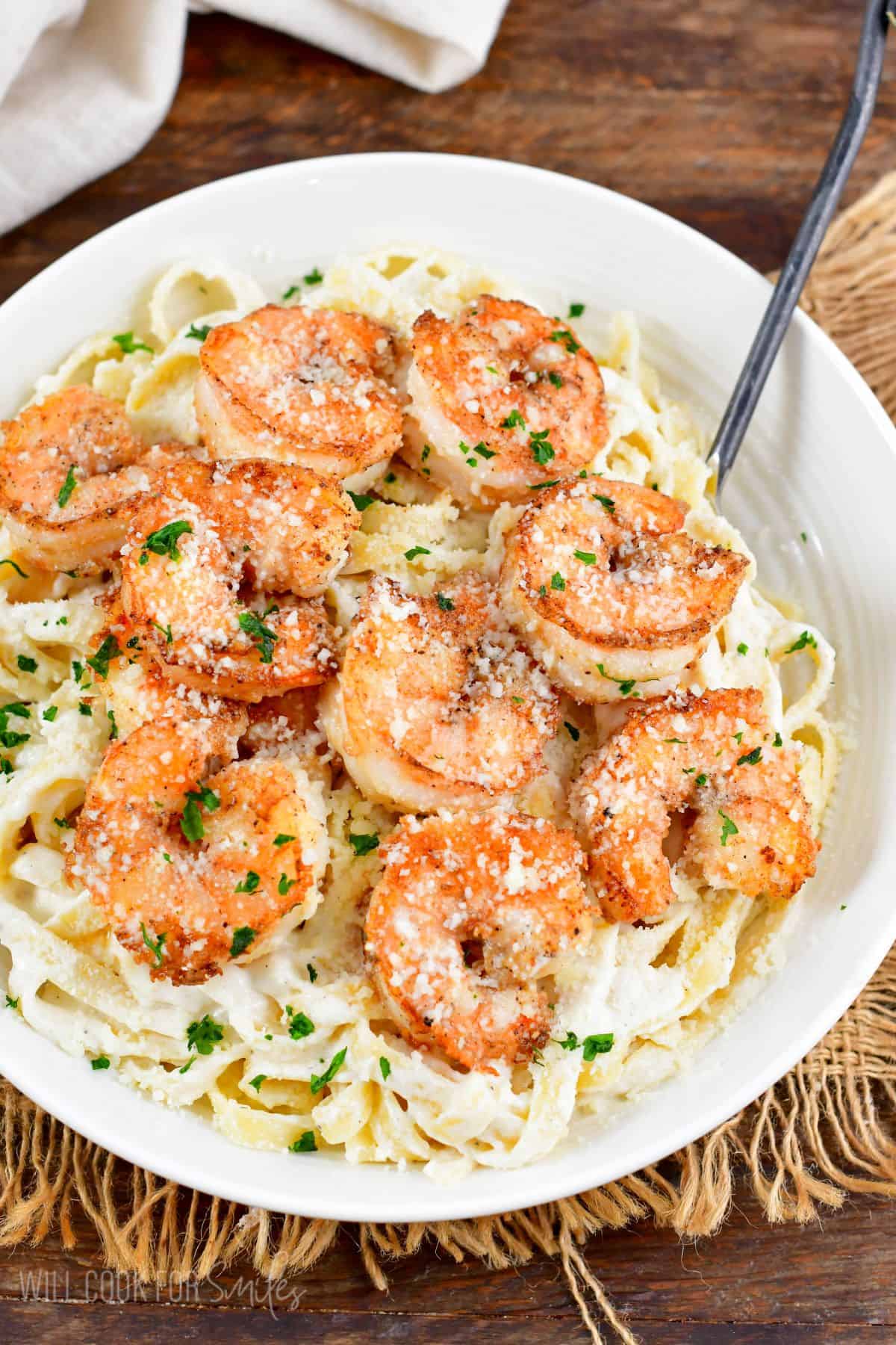 Shrimp alfredo in a bowl on a burlap tablecloth.