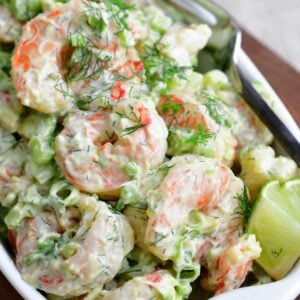 Shrimp salad in a serving dish with lime wedges and dill as garnish.
