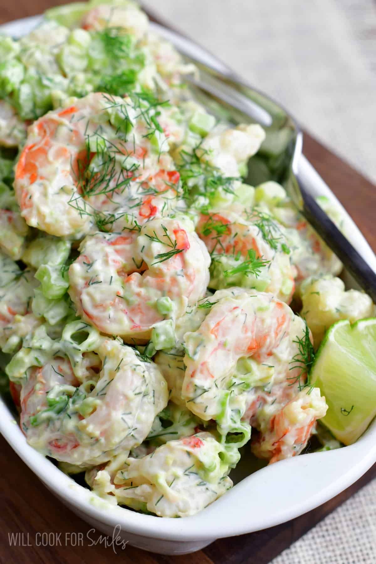 Shrimp salad in a serving dish with lime wedges and dill as garnish.