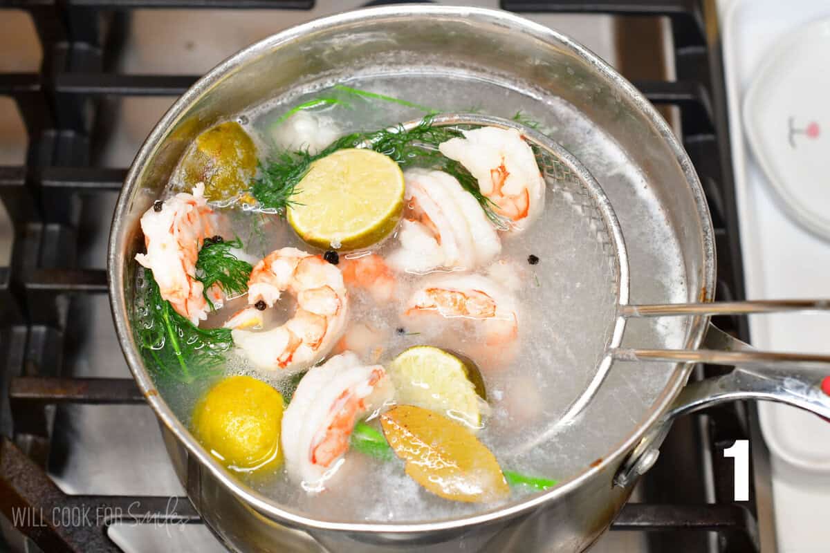 Cooking shrimp salad in a pot with dill and limes and using a metal strainer to mix it.
