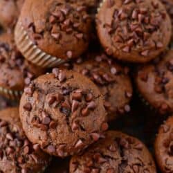 several chocolate banana muffins stacked together next to bananas.