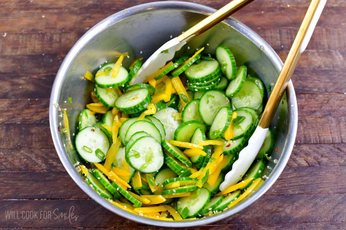 Mixing Asian salad in a in a bowl with a pair of tongs on a wood surface.