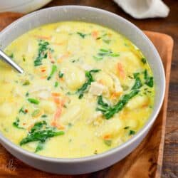 a bowl full of creamy chicken gnocchi soup with a spoon and sitting on a wooden plate.