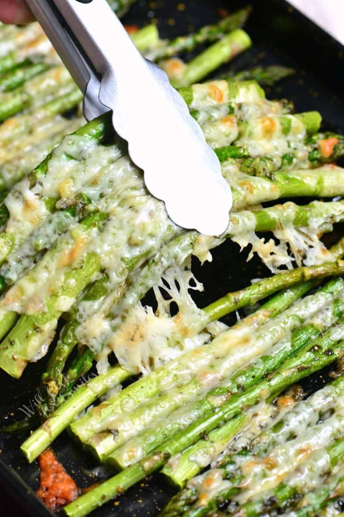pulling out some Italian roasted asparagus with metal tongs from baking sheet.