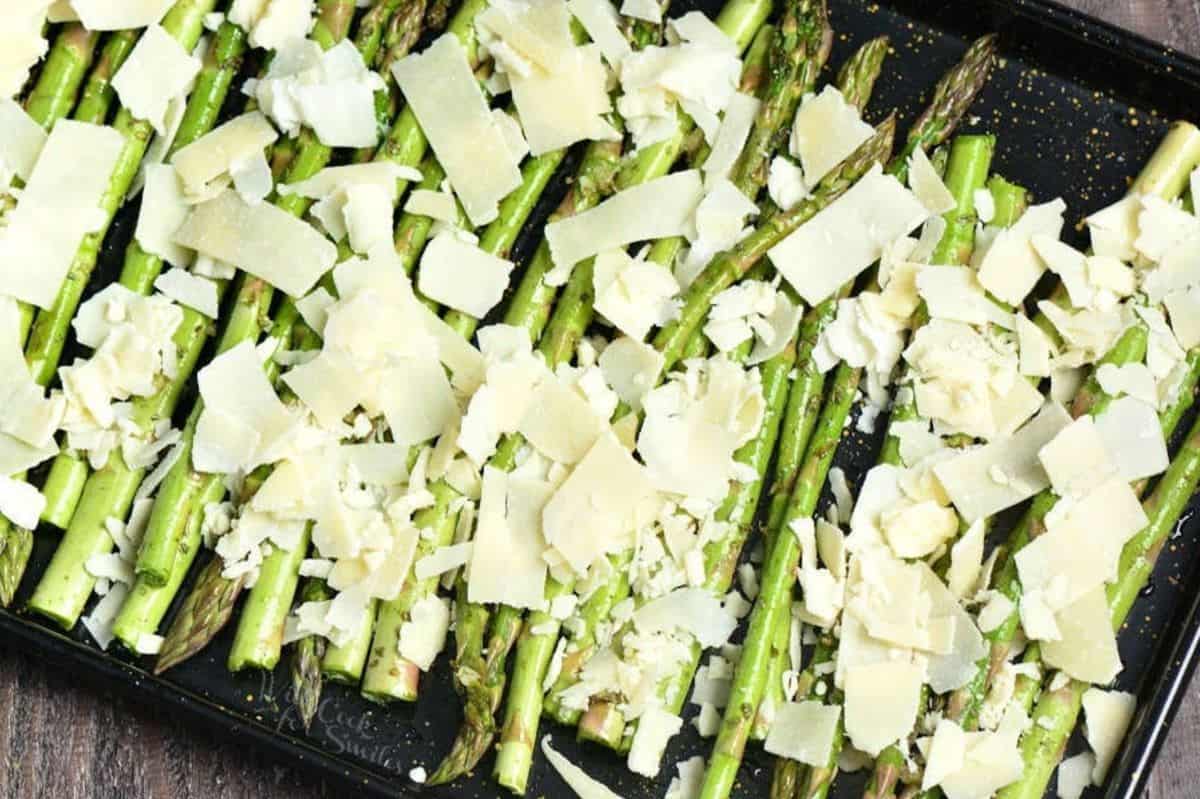 unbaked seasoned asparagus spread in baking pan with shaved parmesan over the top.