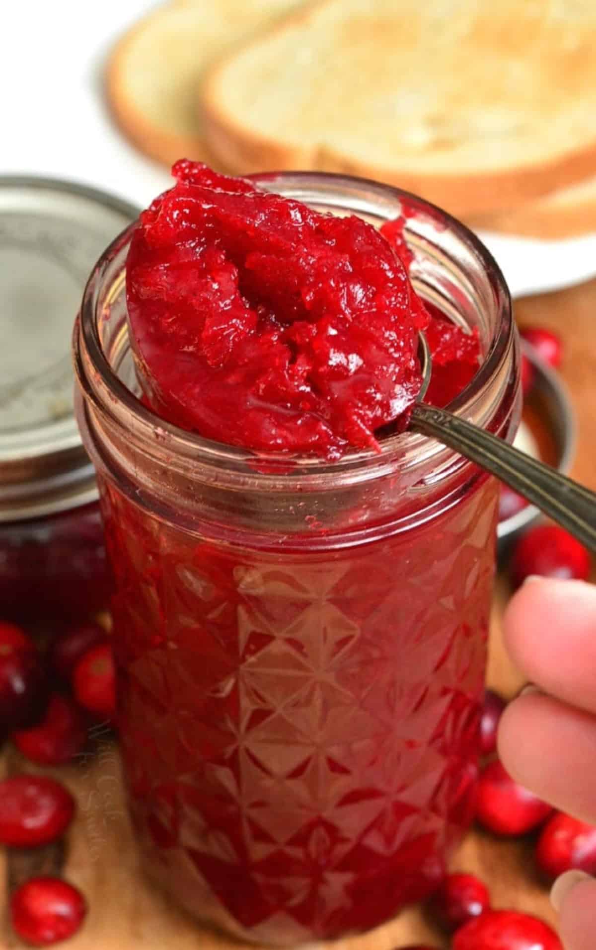 Cranberry jam in a mason jar with a spoon scooping some of the jam out of the jar.