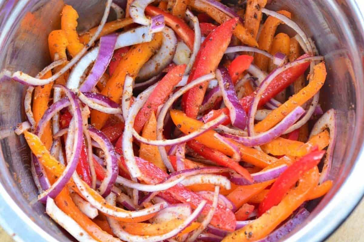 seasoned sliced red onions and red and orange bell peppers in a metal mixing bowl.