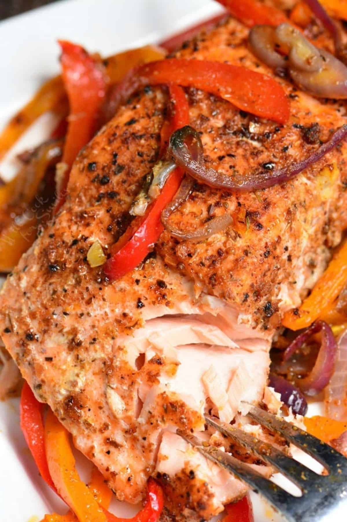 Flavorful Cajun Salmon on a plate with onions and peppers and using a fork to flake apart juicy meat.