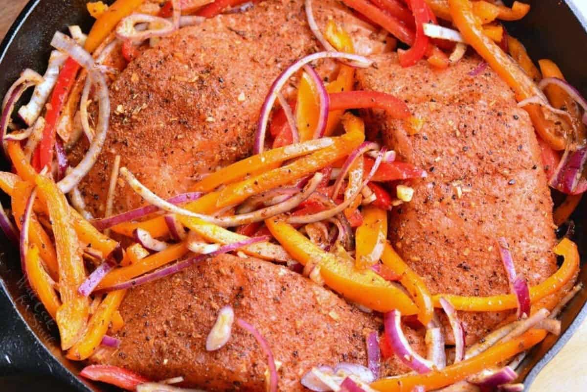 Cajun salmon coated in seasoning, uncooked with seasoned onions and peppers in a skillet.
