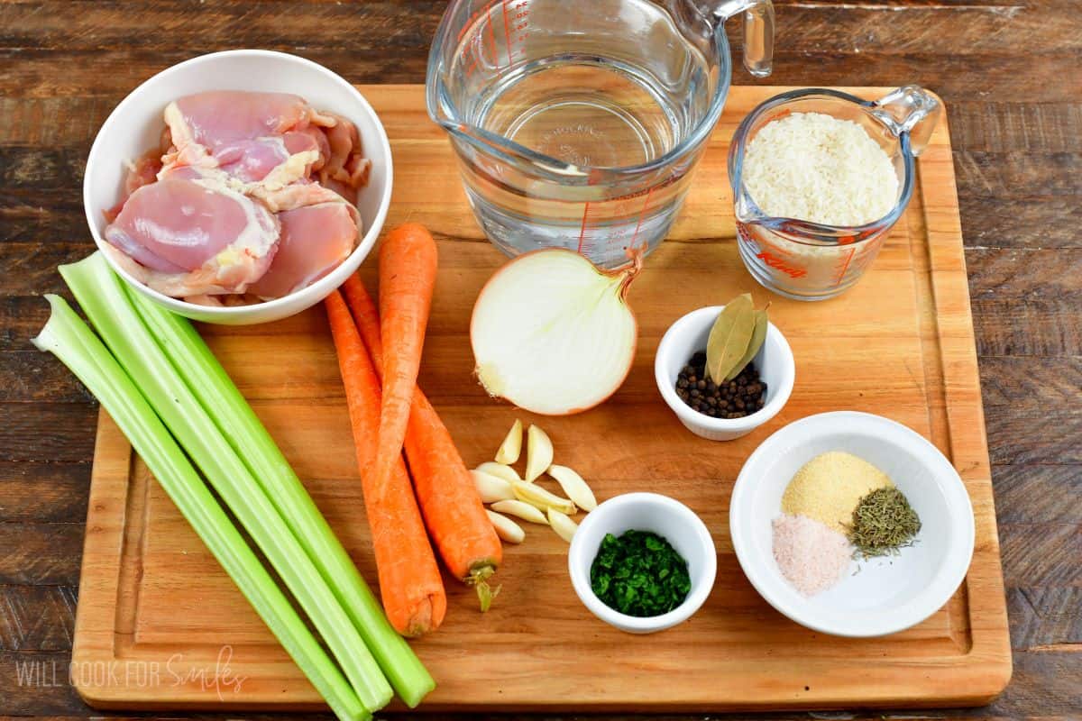 Chicken and rice soup ingredients on a cutting board that is on a wood surface.