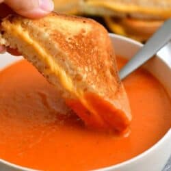 dipping a triangle of grilled cheese into a bowl of tomato soup.