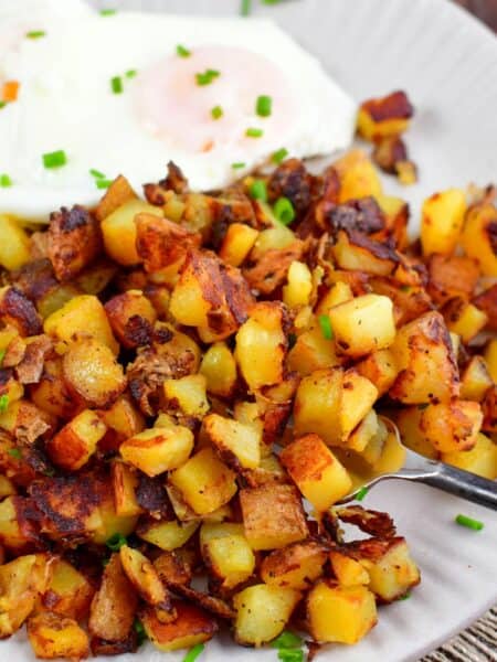 scooping some crispy home fries from the plate using a fork.