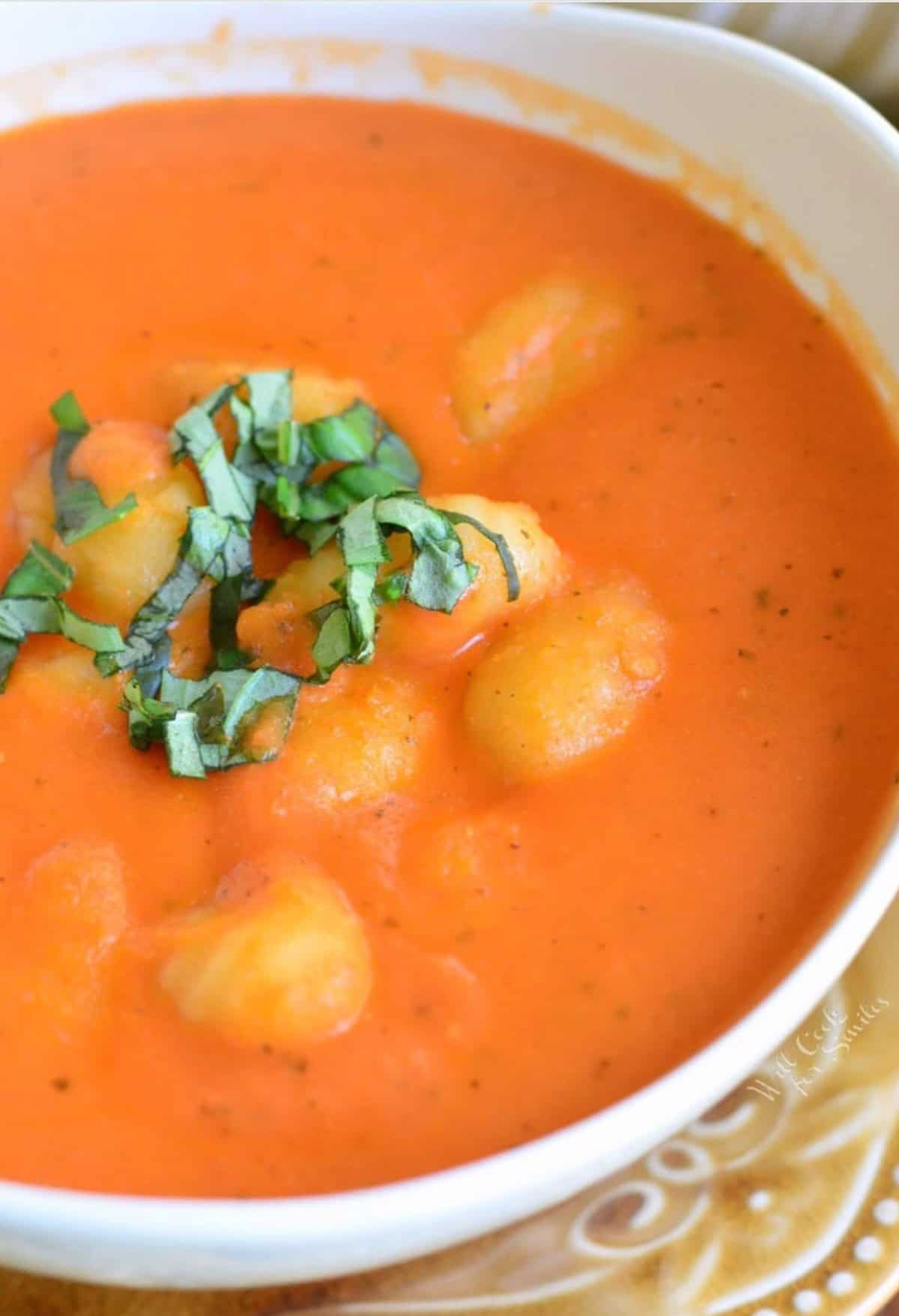Tomato soup with gnocchi in a bowl with a spoon and basil sprinkled on top as garnish.