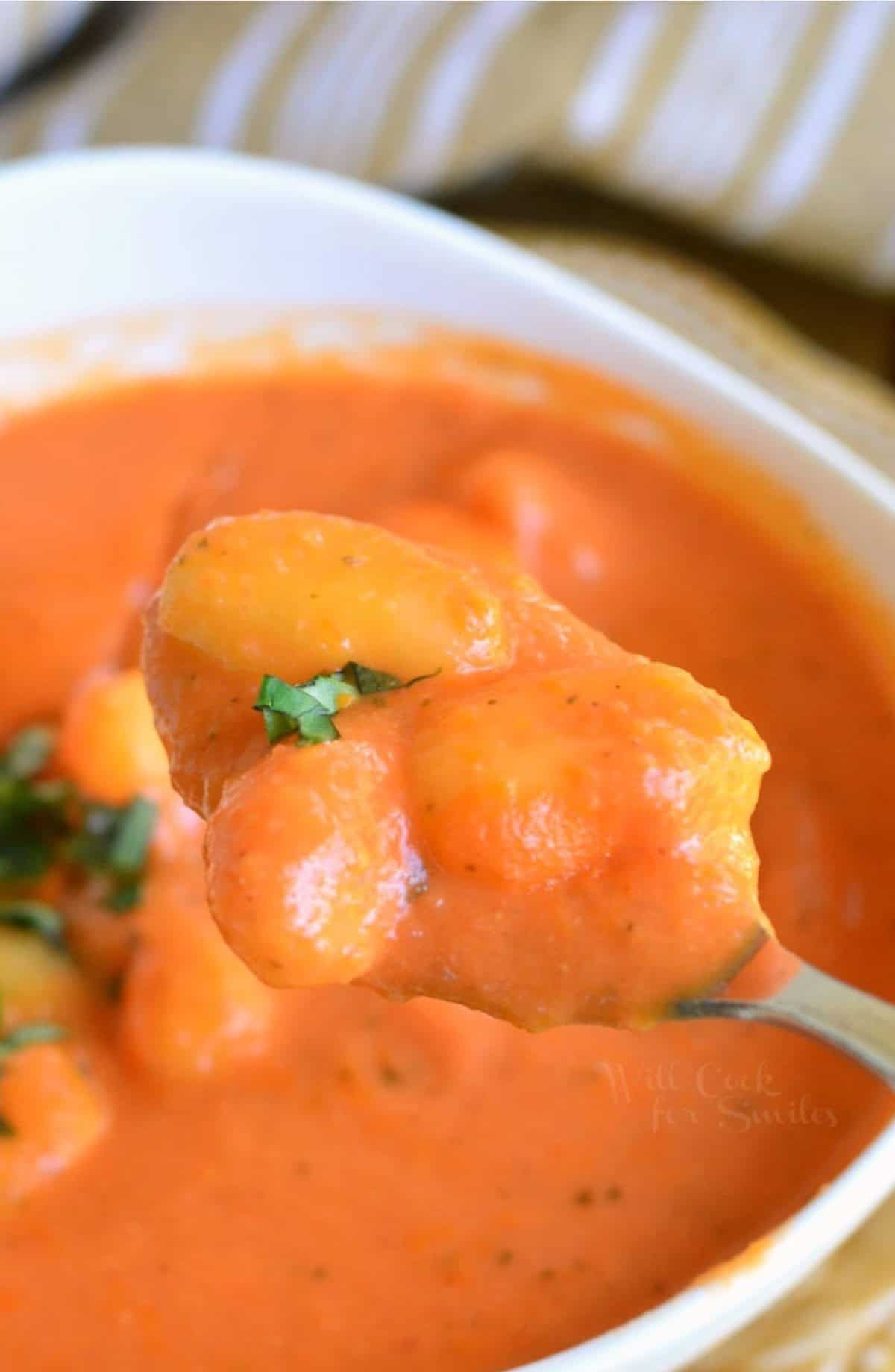 Homemade tomato soup with gnocchi scooped on a spoon from a bowl.