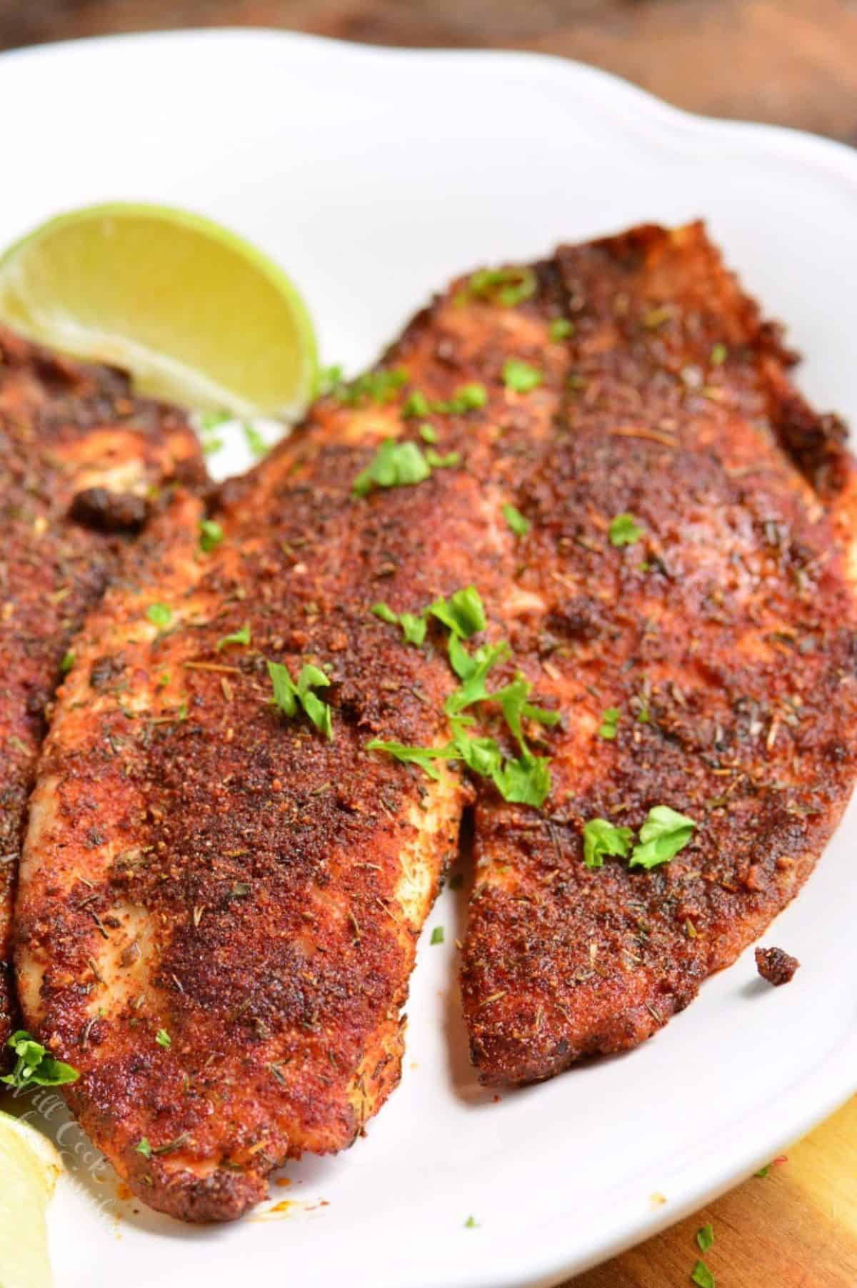 Blackened tilapia on a white plate with a slice of lime.