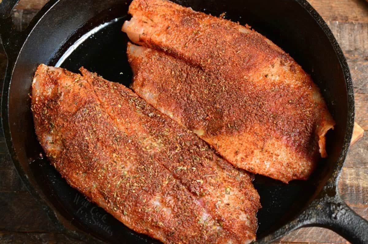 two uncooked blackened tilpa filets in a cast iron skillet.