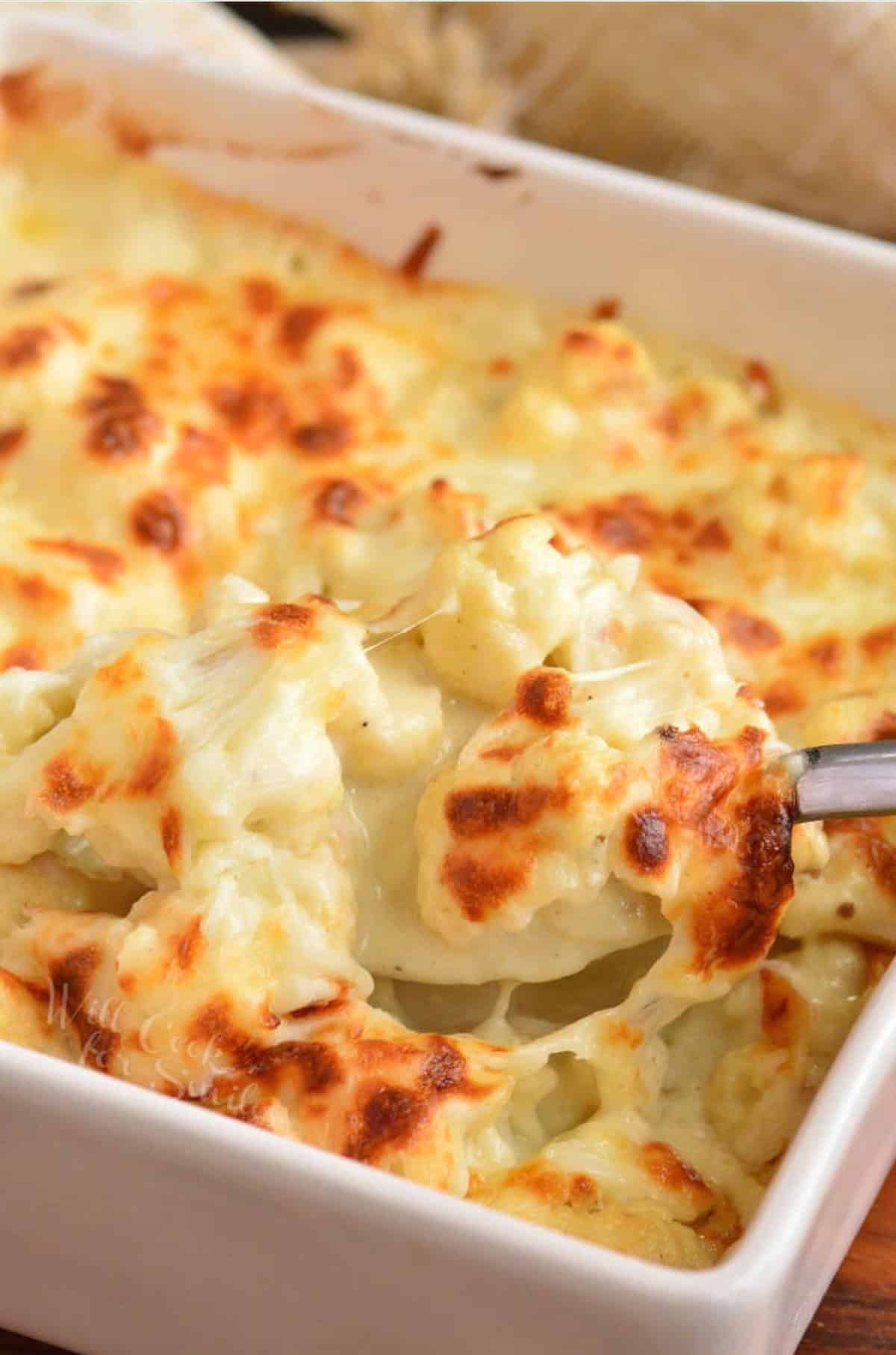 Scooping cauliflower mac and cheese out of a baking dish.