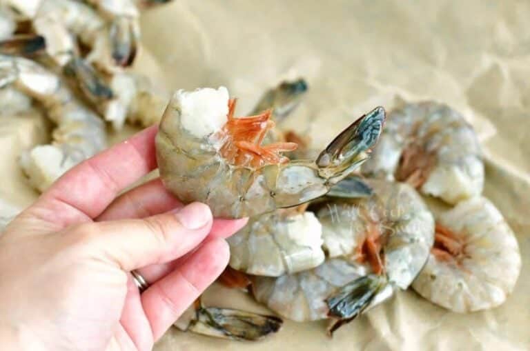 Holding a whole shrimp while the rest of the shrimp are on parchement paper.