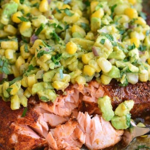 flaked baked salmon on a fork next to salmon filet with avocado corn topping.