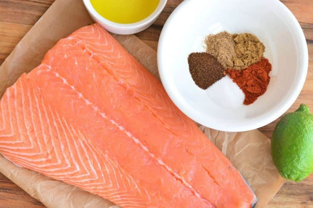 salmon filet, seasoning mix, lime, and butter on a cutting board.