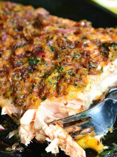 cutting into the grilled salmon in a skillet with a fork and citrus sauce on top.